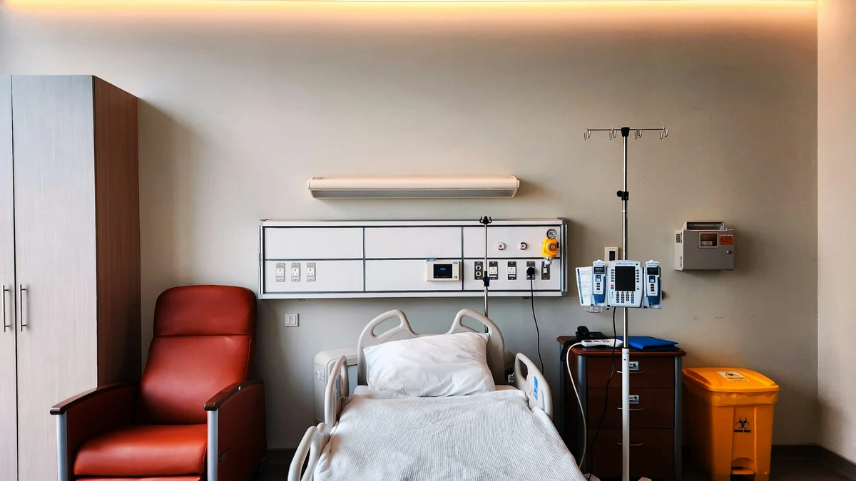Empty hospital room with a bed, a recliner chair and bedside equipment